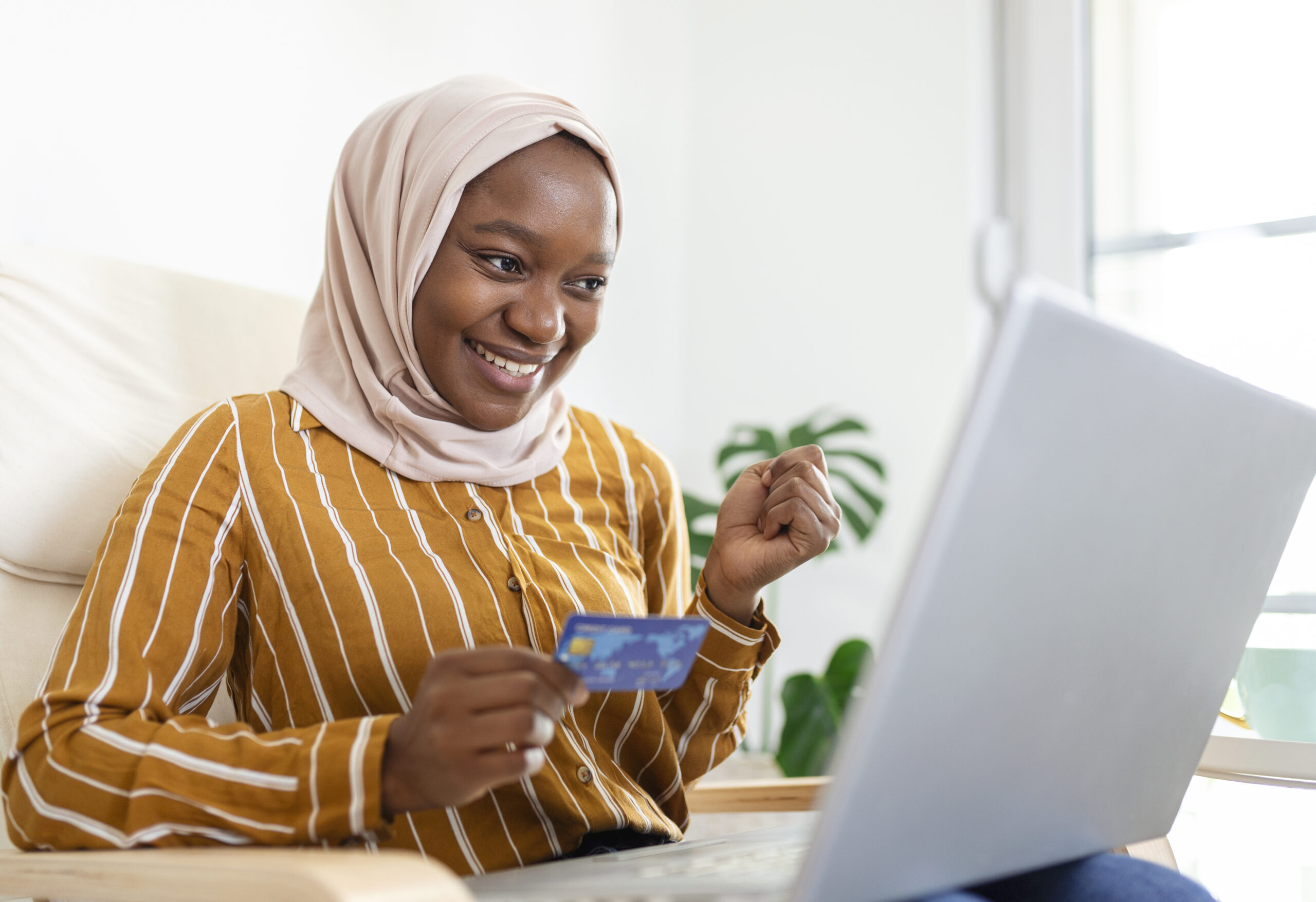 Elegant attractive Muslim woman using mobile laptop searching online shopping information in living room at home. Portrait of happy woman purchasing product via online shopping. Pay using credit card